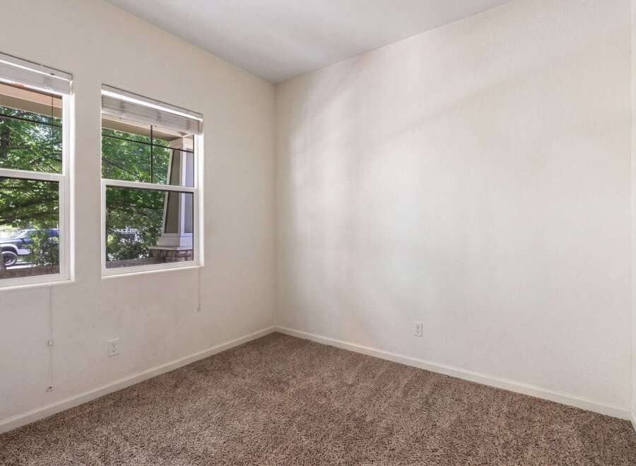 This empty room features a neutral color palette with beige carpeting and off-white walls, creating a blank canvas for personalization.
