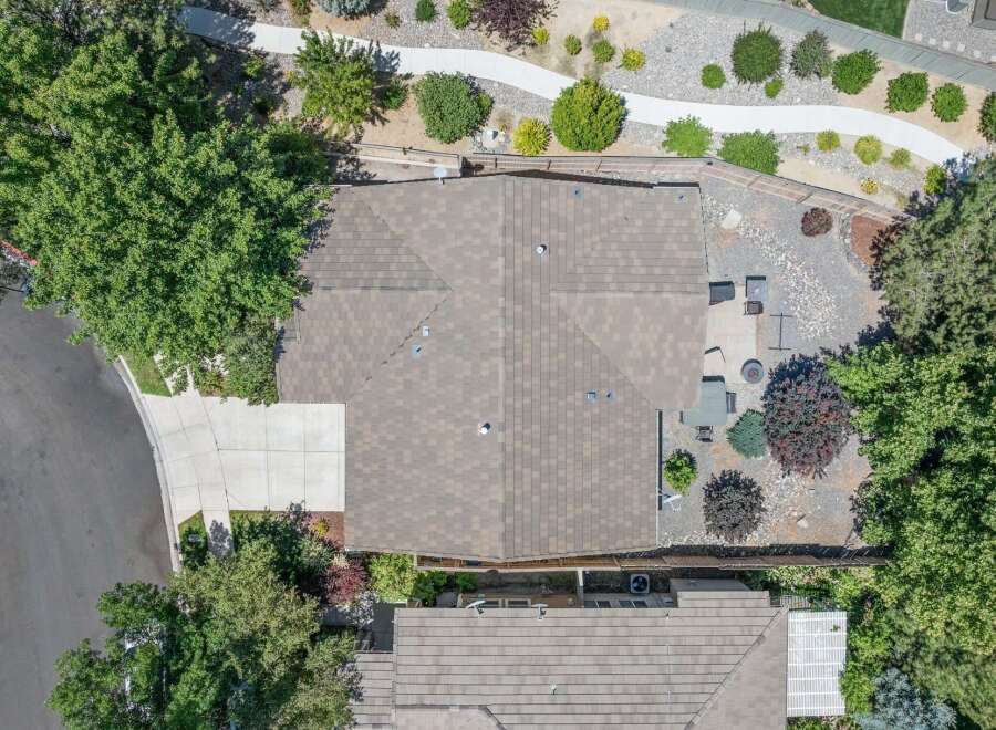 Discover this stunning aerial view showcasing a beautifully maintained property with a spacious, well-kept roof and a paved driveway leading to the home.