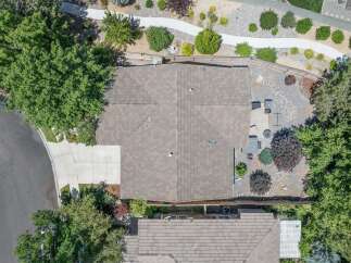 Discover this stunning aerial view showcasing a beautifully maintained property with a spacious, well-kept roof and a paved driveway leading to the home.