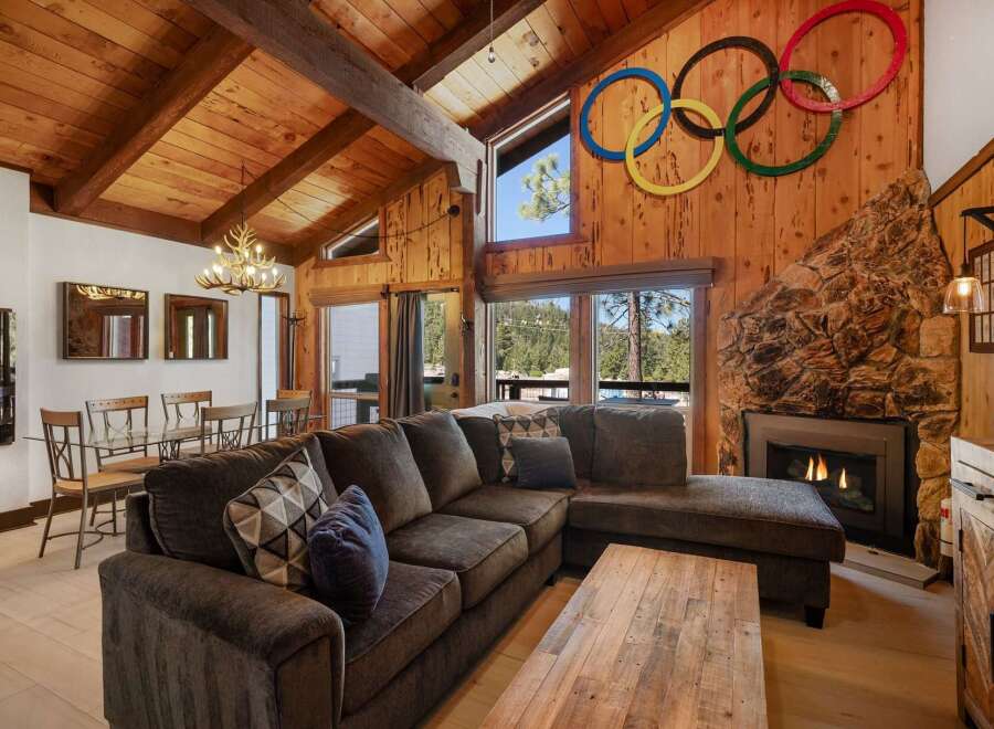 Experience rustic charm in this mountain lodge living room, featuring a grand stone fireplace and a vaulted wood-paneled ceiling with exposed beams.