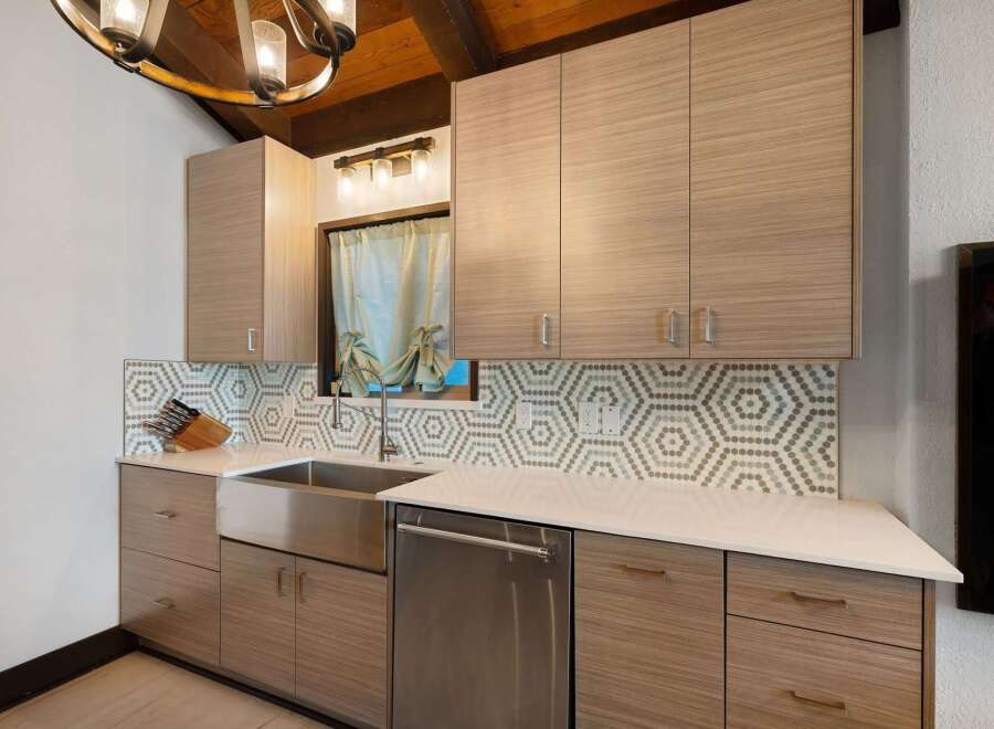 This modern kitchen features sleek, light wood cabinetry with minimalist hardware, complemented by a striking hexagonal tile backsplash.