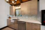 This modern kitchen features sleek, light wood cabinetry with minimalist hardware, complemented by a striking hexagonal tile backsplash.