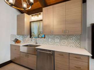 This modern kitchen features sleek, light wood cabinetry with minimalist hardware, complemented by a striking hexagonal tile backsplash.