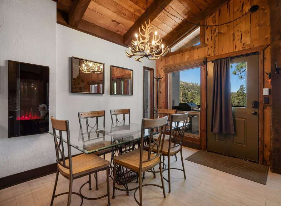 Experience rustic charm in this dining area featuring a unique antler chandelier and a sleek glass-top table.