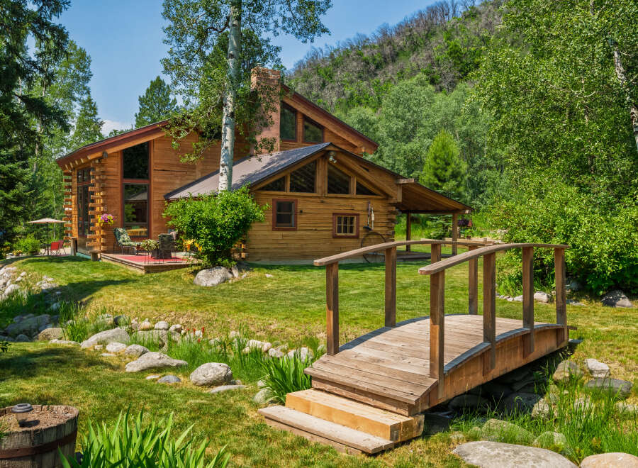 Experience rustic charm in this stunning log cabin nestled amidst lush greenery and a serene water feature.