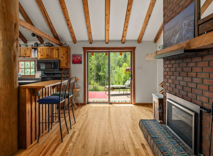 Experience rustic charm in this cozy cabin kitchen featuring warm wood cabinetry, a breakfast bar with seating, and a stunning view of the surrounding greenery through a large sliding glass door.