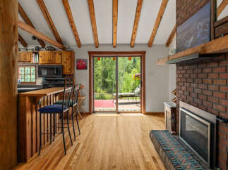 Experience rustic charm in this cozy cabin kitchen featuring warm wood cabinetry, a breakfast bar with seating, and a stunning view of the surrounding greenery through a large sliding glass door.