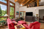 Experience rustic charm in this spacious living room featuring a vaulted wood-beamed ceiling and large windows offering serene forest views.