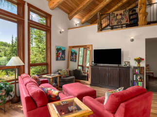 Experience rustic charm in this spacious living room featuring a vaulted wood-beamed ceiling and large windows offering serene forest views.