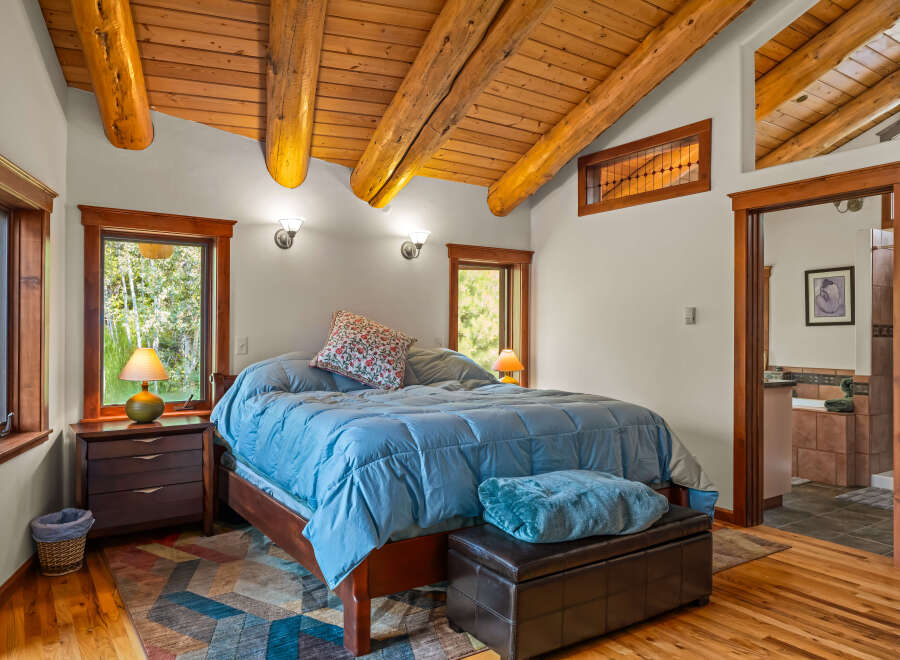Experience rustic charm in this inviting bedroom featuring a vaulted wood-beamed ceiling and large windows offering serene views.