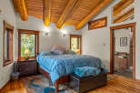 Experience rustic charm in this inviting bedroom featuring a vaulted wood-beamed ceiling and large windows offering serene views.