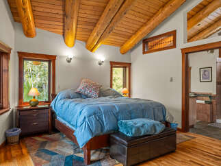 Experience rustic charm in this inviting bedroom featuring a vaulted wood-beamed ceiling and large windows offering serene views.