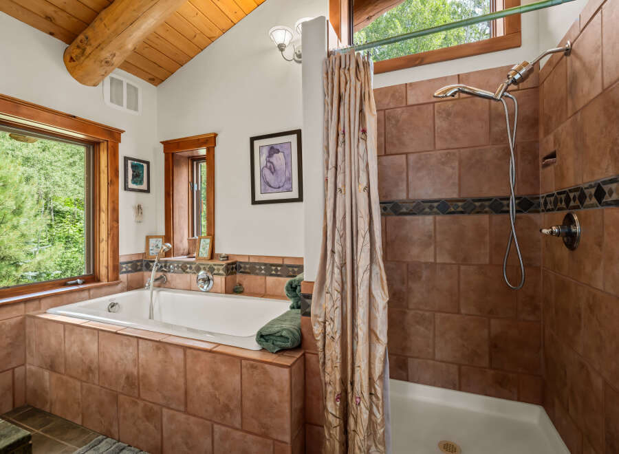 Experience tranquility in this rustic bathroom featuring a deep soaking tub surrounded by warm terracotta tiles and a separate shower with elegant tilework.