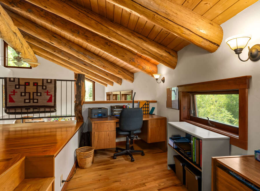 Discover a charming loft office space with rustic log beam accents and a vaulted wood-paneled ceiling.