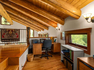 Discover a charming loft office space with rustic log beam accents and a vaulted wood-paneled ceiling.