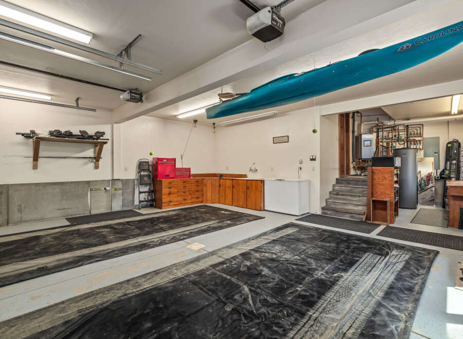 This spacious garage offers ample storage and organization solutions, featuring overhead shelving for equipment and a large wooden cabinet unit with multiple drawers.