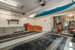 This spacious garage offers ample storage and organization solutions, featuring overhead shelving for equipment and a large wooden cabinet unit with multiple drawers.