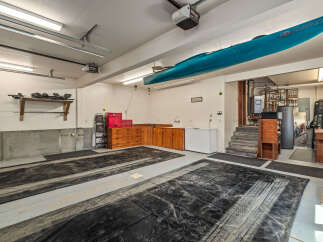 This spacious garage offers ample storage and organization solutions, featuring overhead shelving for equipment and a large wooden cabinet unit with multiple drawers.