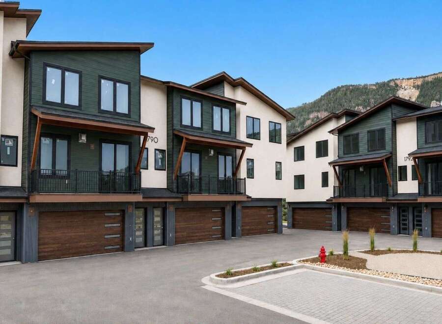 Discover modern living in these stunning townhomes featuring sleek dark green and cream exteriors, complemented by rich wood garage doors.