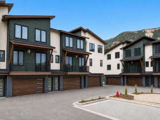 Discover modern living in these stunning townhomes featuring sleek dark green and cream exteriors, complemented by rich wood garage doors.