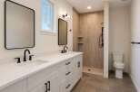 This modern bathroom features a spacious double vanity with white quartz countertops and sleek black fixtures.