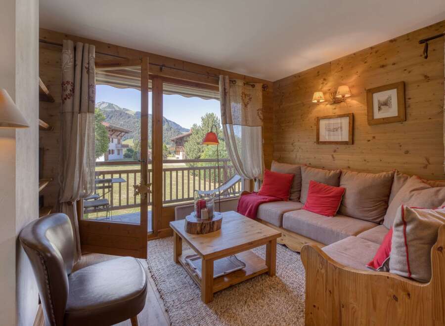 Experience cozy mountain living in this charming living room featuring warm wood paneling and a comfortable sectional sofa adorned with red accent pillows.