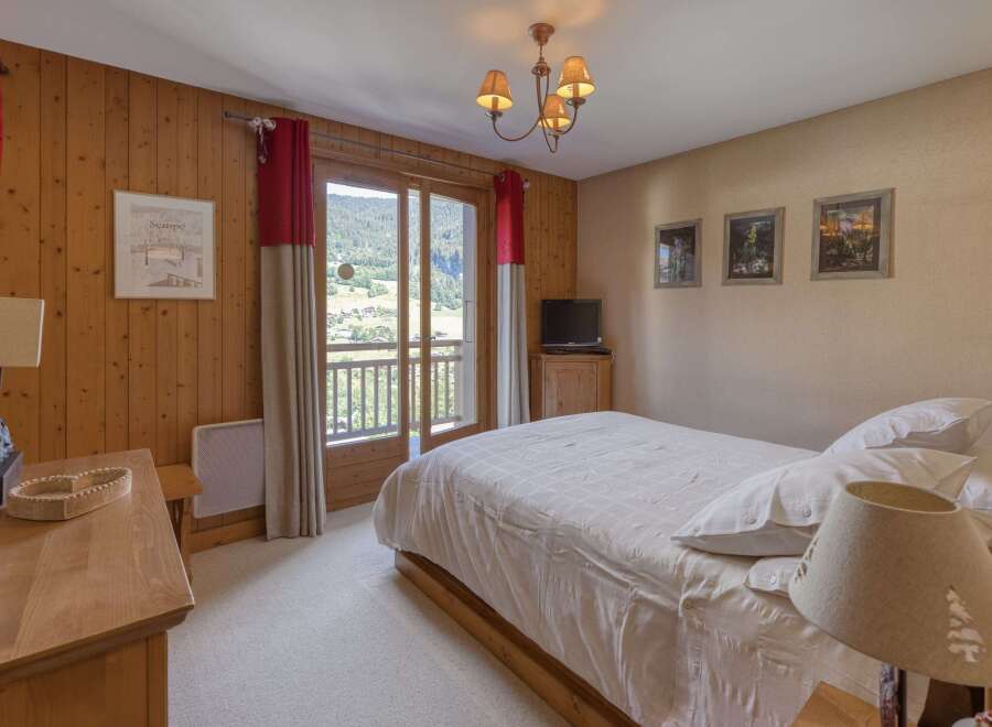 Experience serene mountain living in this charming bedroom featuring warm wood paneling and a private balcony with breathtaking views.