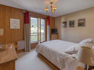 Experience serene mountain living in this charming bedroom featuring warm wood paneling and a private balcony with breathtaking views.