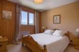 Experience breathtaking mountain views from this charming bedroom, featuring a cozy wooden bed and large windows that frame the stunning alpine scenery.
