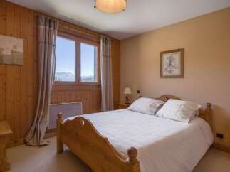 Experience breathtaking mountain views from this charming bedroom, featuring a cozy wooden bed and large windows that frame the stunning alpine scenery.
