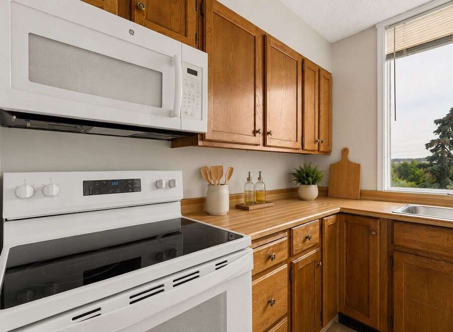 This charming kitchen features warm oak cabinetry complemented by a sleek white microwave and range.