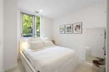 Experience modern comfort in this bright bedroom, featuring a plush white duvet and a large window offering serene views of lush greenery.