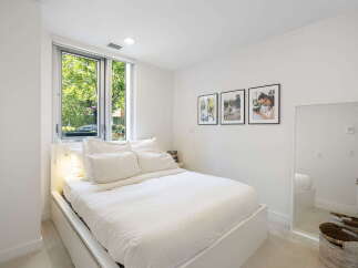 Experience modern comfort in this bright bedroom, featuring a plush white duvet and a large window offering serene views of lush greenery.