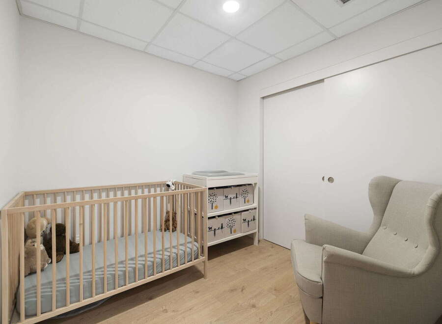 This nursery features a light wood crib with stuffed animals, a changing table with storage drawers, and a comfortable armchair.
