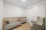 This nursery features a light wood crib with stuffed animals, a changing table with storage drawers, and a comfortable armchair.