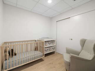 This nursery features a light wood crib with stuffed animals, a changing table with storage drawers, and a comfortable armchair.
