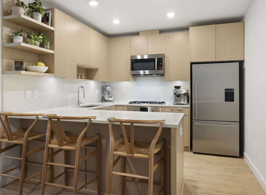 This modern kitchen features sleek, light wood cabinetry and a spacious quartz countertop island, perfect for casual dining or entertaining.