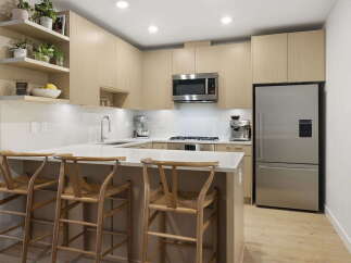 This modern kitchen features sleek, light wood cabinetry and a spacious quartz countertop island, perfect for casual dining or entertaining.