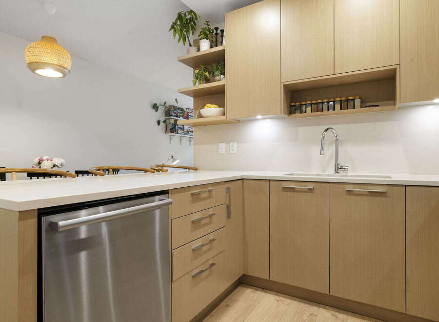 This modern kitchen features sleek, light wood cabinetry and a durable quartz countertop, perfect for meal preparation.