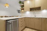 This modern kitchen features sleek, light wood cabinetry and a durable quartz countertop, perfect for meal preparation.