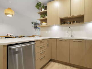 This modern kitchen features sleek, light wood cabinetry and a durable quartz countertop, perfect for meal preparation.