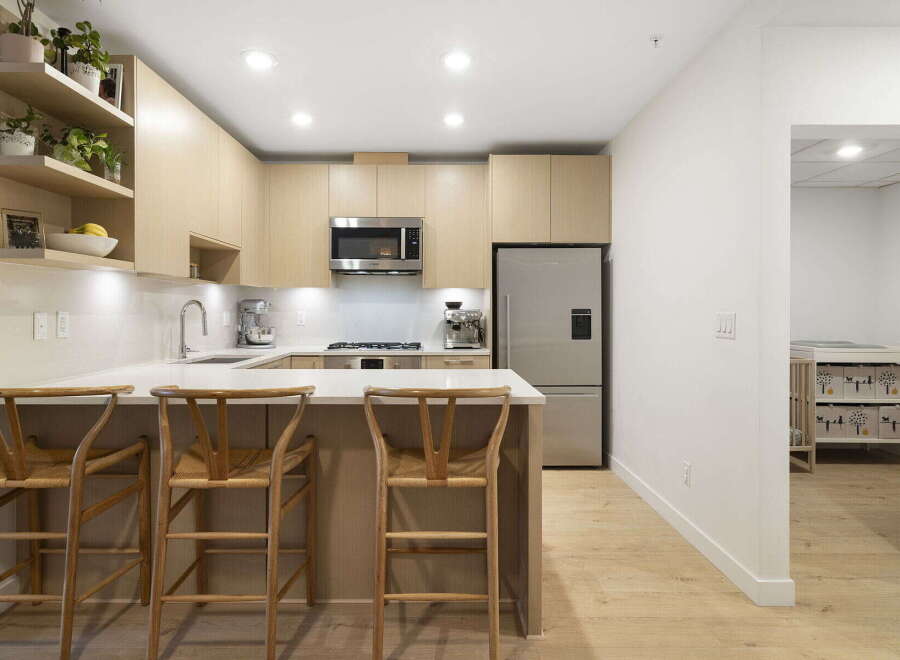 This modern kitchen boasts sleek, light wood cabinetry and a spacious quartz countertop, perfect for meal preparation and casual dining.