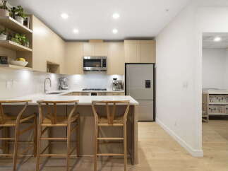 This modern kitchen boasts sleek, light wood cabinetry and a spacious quartz countertop, perfect for meal preparation and casual dining.