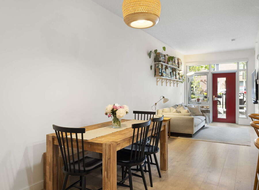 Bright and airy open-concept living space featuring a modern dining area with a wooden table and chairs, adjacent to a comfortable living room with a plush sofa.