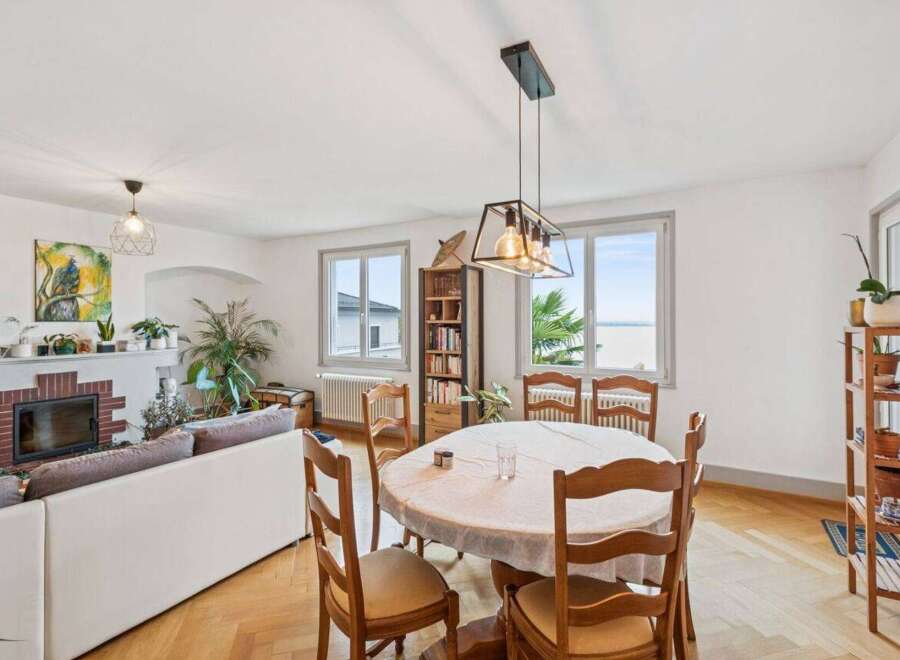 This spacious living and dining area features a cozy fireplace, a comfortable white sofa, and a charming round dining table perfect for family meals.