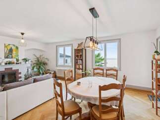 This spacious living and dining area features a cozy fireplace, a comfortable white sofa, and a charming round dining table perfect for family meals.