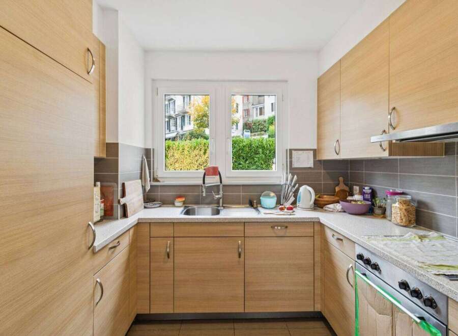 This modern kitchen features sleek, light wood cabinetry and a bright, airy feel, enhanced by a large window overlooking lush greenery.