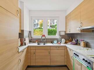 This modern kitchen features sleek, light wood cabinetry and a bright, airy feel, enhanced by a large window overlooking lush greenery.