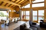 Experience breathtaking mountain views from this stunning wooden chalet, featuring a spacious dining area with a large wooden table and modern white chairs.