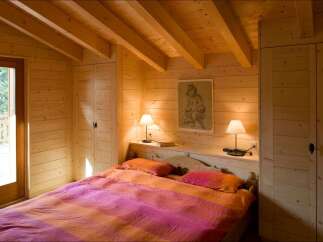 Experience rustic charm in this cozy wooden bedroom, featuring a comfortable bed with vibrant bedding and a beautiful piece of art above the headboard.